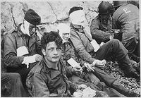 Après l'attaque de la plage d'Omaha, les blessés des troupes d'assaut américaines du 16ème Régiment d'Infanterie attendent adossés aux falaises de craie l'évacuation vers un hôpital de campagne.(National Archives)